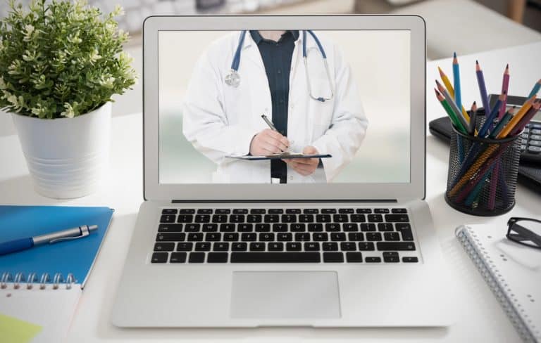 Laptop showing a doctor in white coat with stethoscope and clipboard.